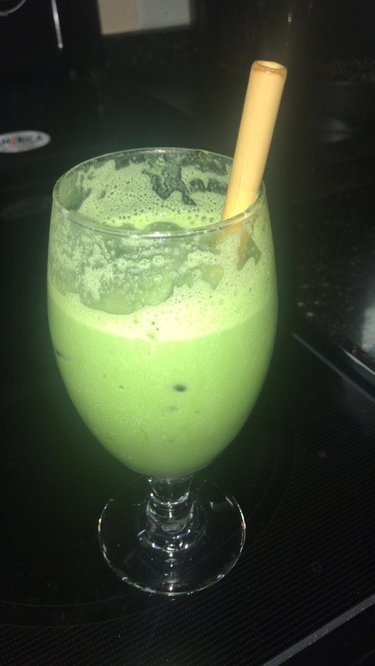 A green drink is in a glass with a straw.